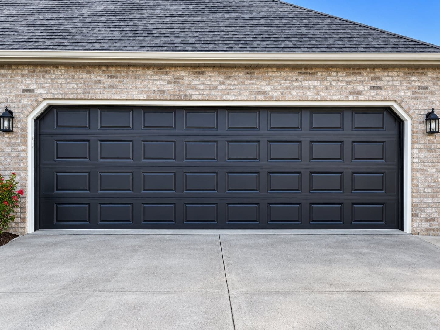 A black raised-panel double garage door in a brick wall