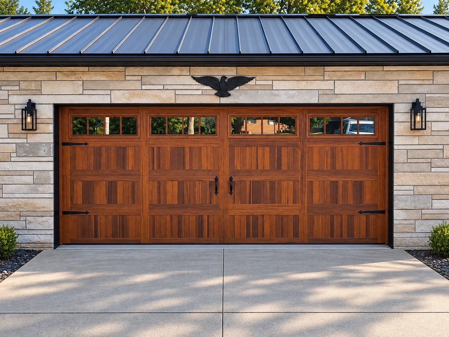 A walnut-finish carriage-house garage door with a row of windows, set in a limestone wall under a standing-seam roof