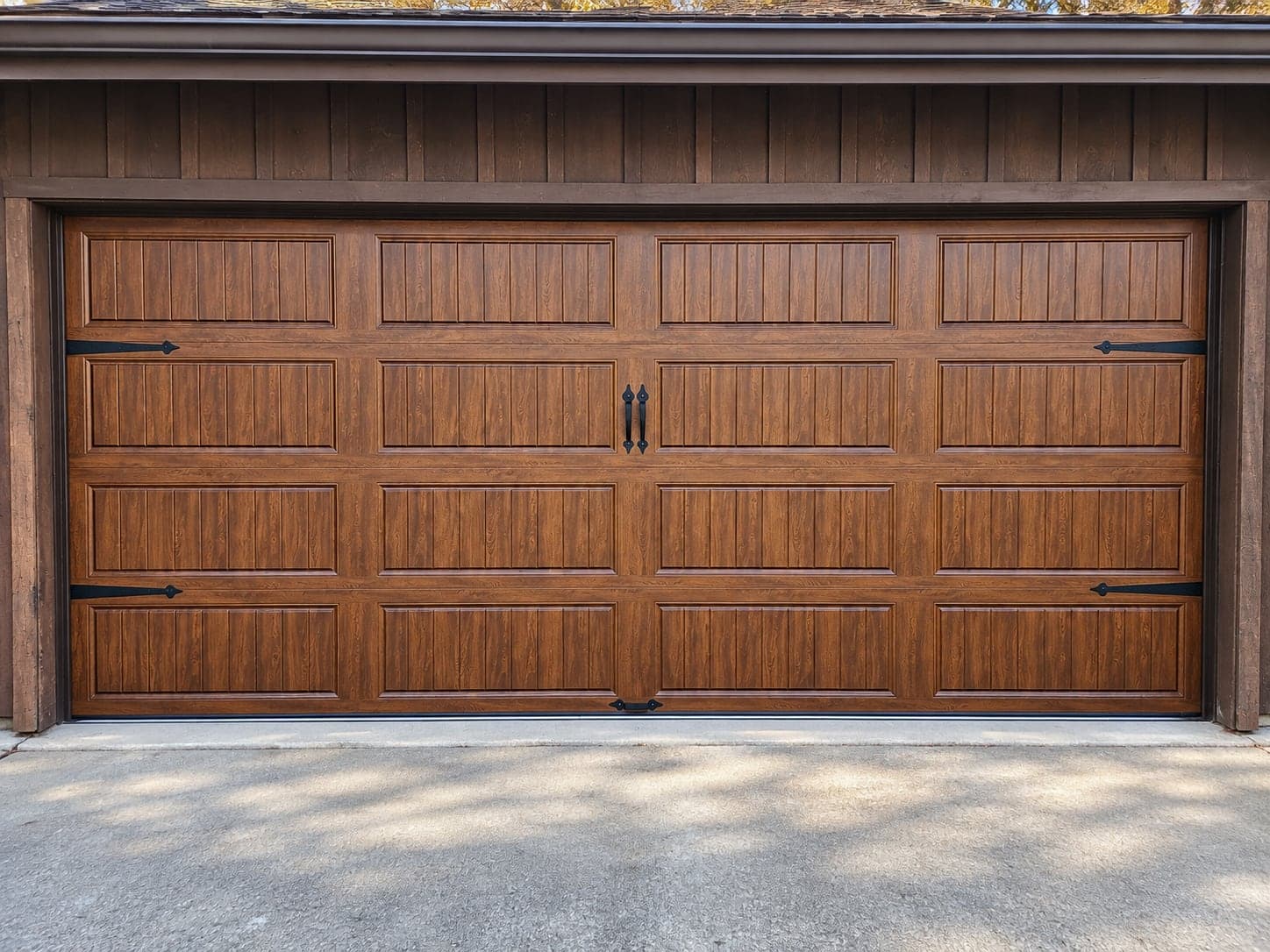 Close view of a woodgrain carriage-house garage door with black strap hinges and handles